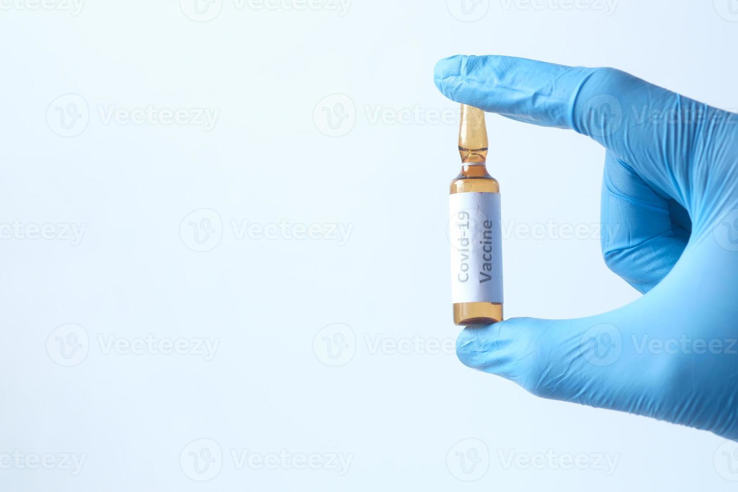 Mano en guantes de látex con vacuna en ampolla de vidrio foto