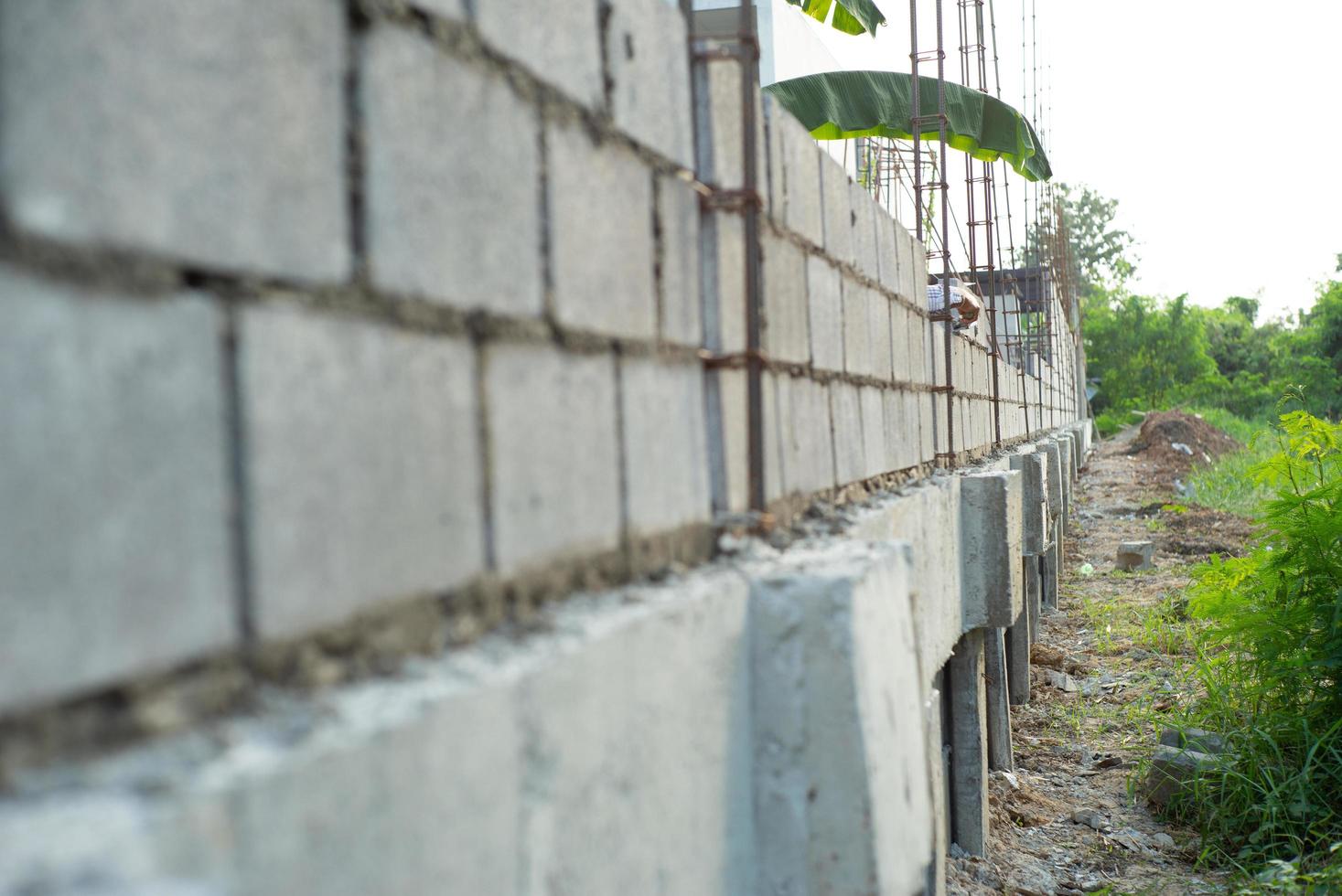 Paisaje del sitio de construcción con muro de albañil de hormigón y la mano del trabajador instalando los ladrillos en la pared de fondo. foto