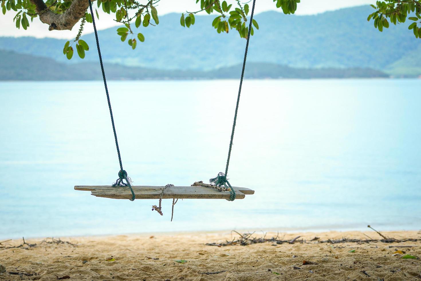 Closeup wooden swing hanging from the tree with old rope and blurred island in background photo