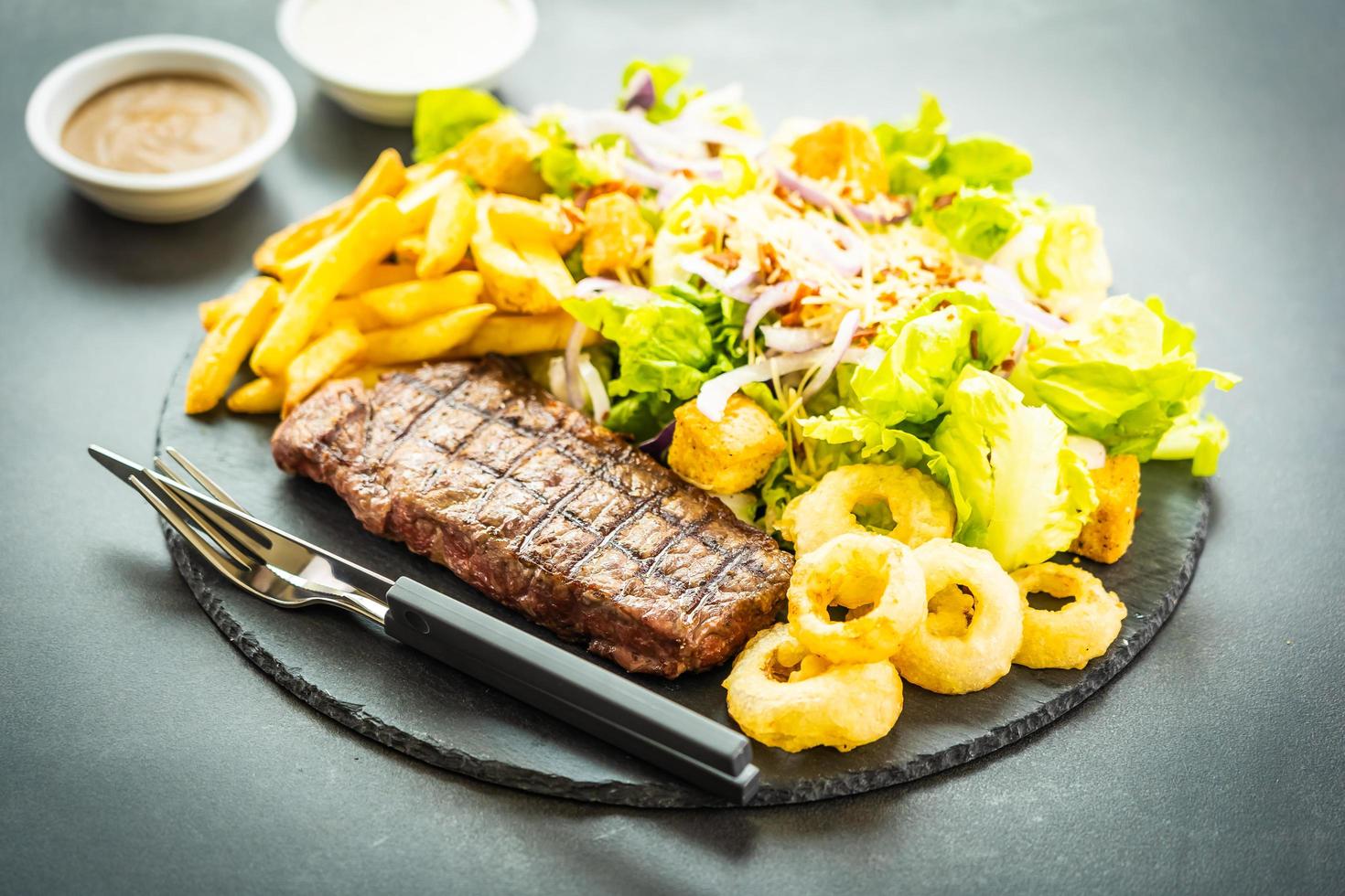 Grilled beef meat steak with french fries onion ring with sauce and fresh vegetable photo