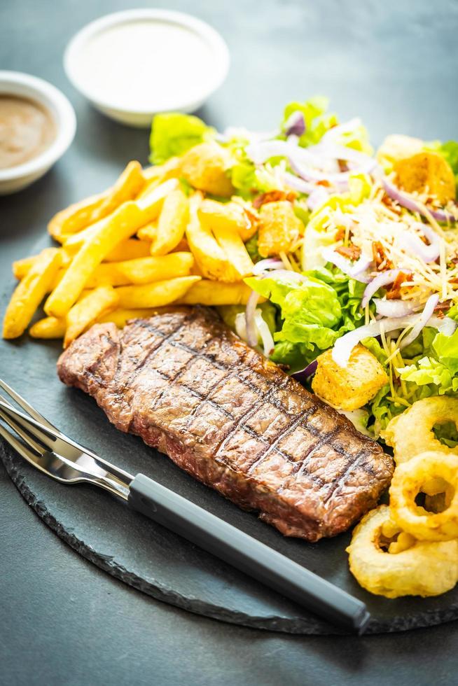 Grilled beef meat steak with french fries onion ring with sauce and fresh vegetable photo