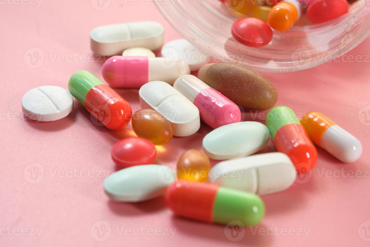 Close up of many colorful pills and capsules spilling on pink background photo