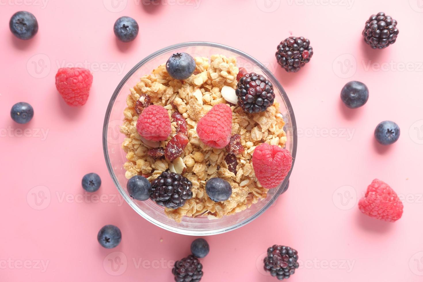 granola y bayas en un tazón sobre fondo rosa foto