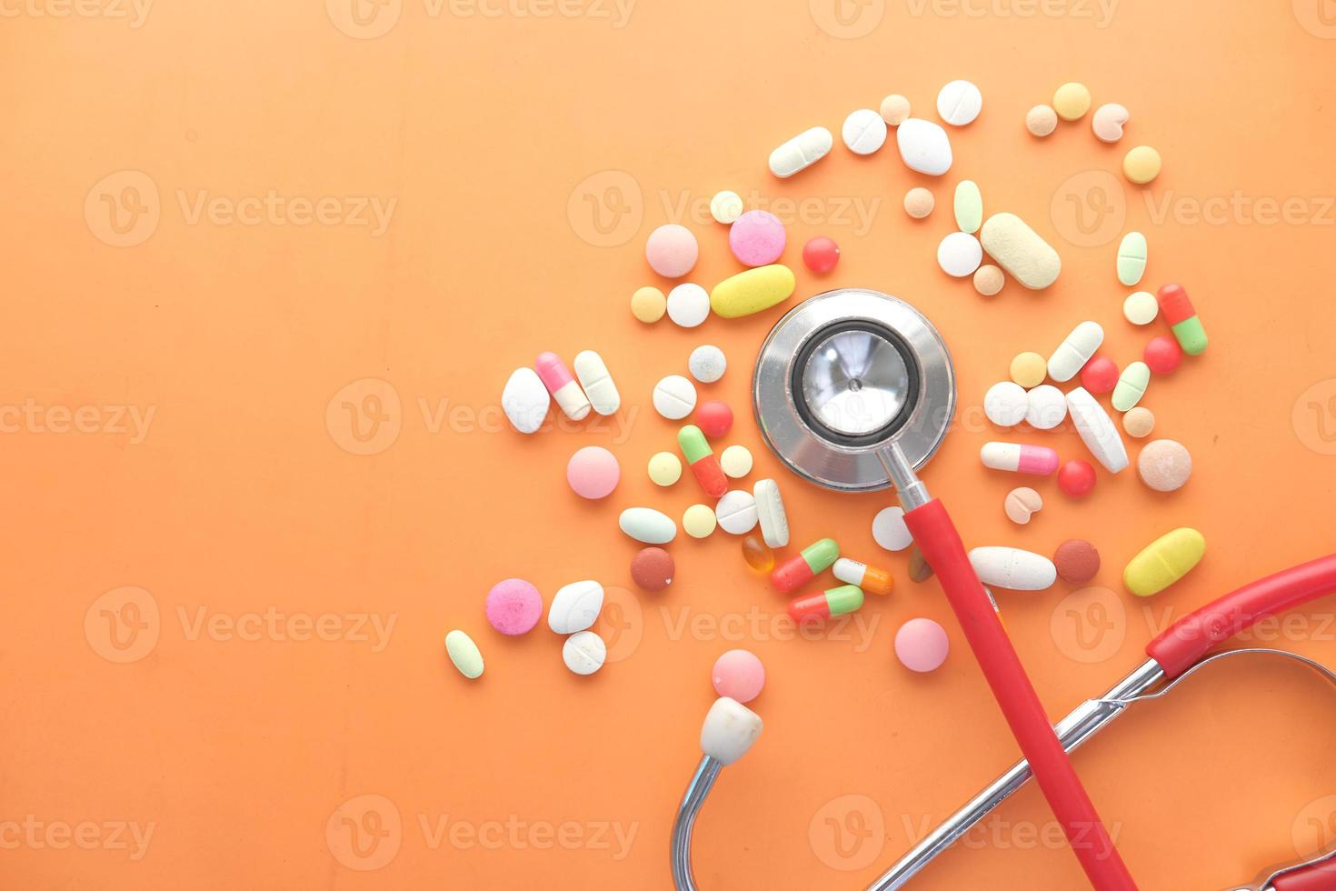 Coloridas píldoras médicas y un estetoscopio sobre fondo naranja foto