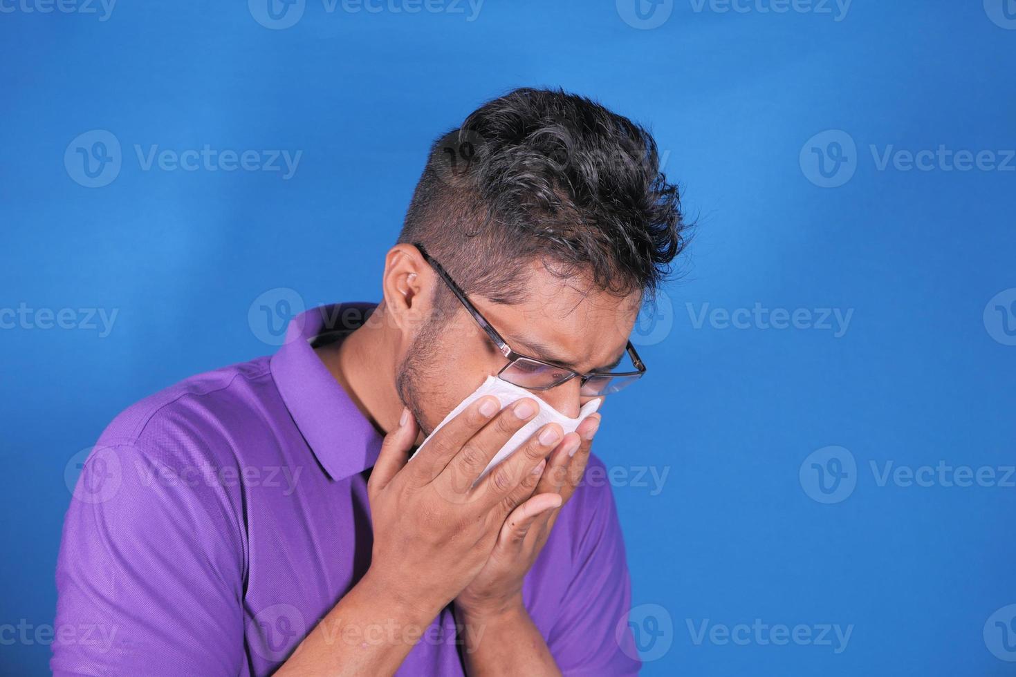 Hombre de camisa morada estornudando sobre fondo azul. foto