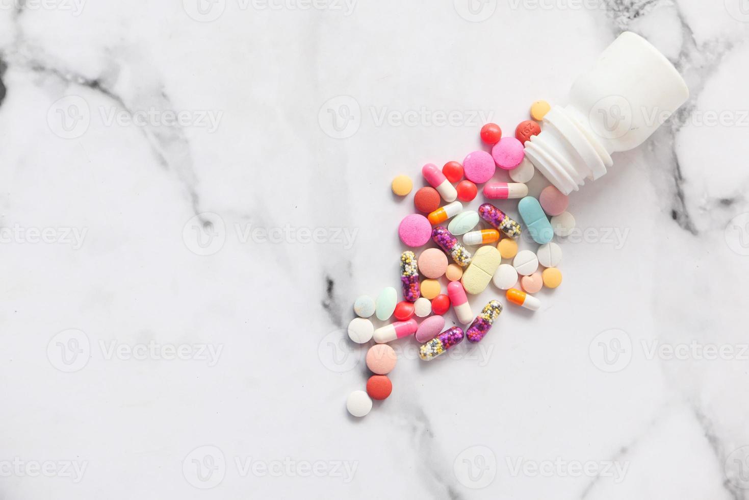 Colorful pills spilling on white marble background photo