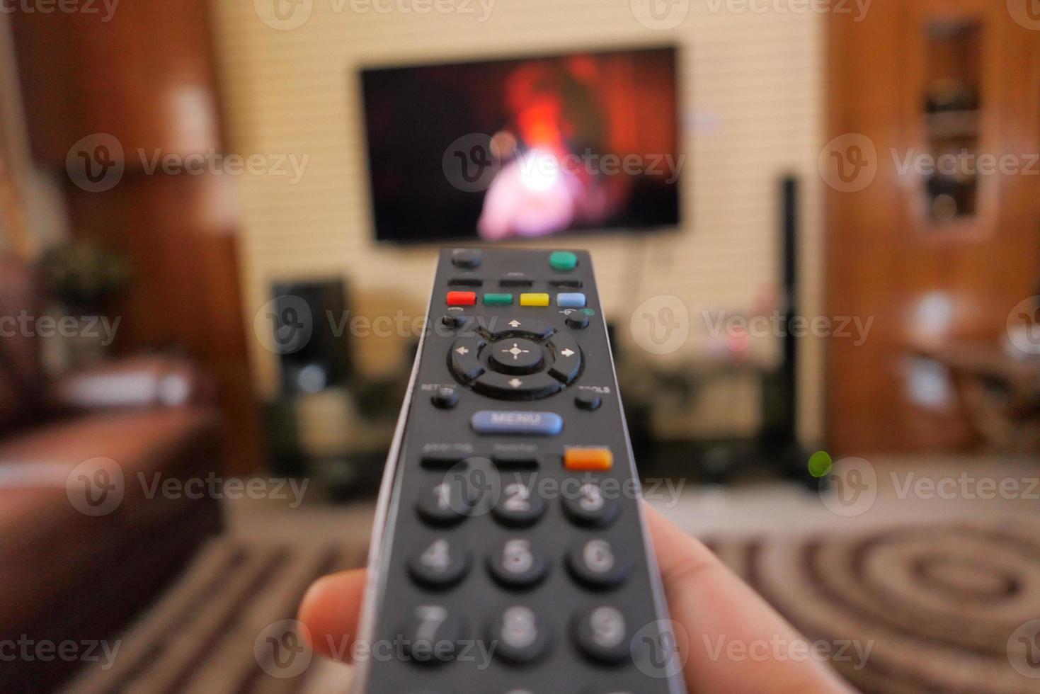 Hand holding TV remote in a living room photo