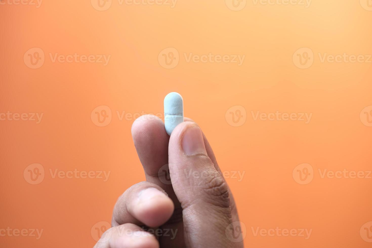 Holding blue pill on orange background photo