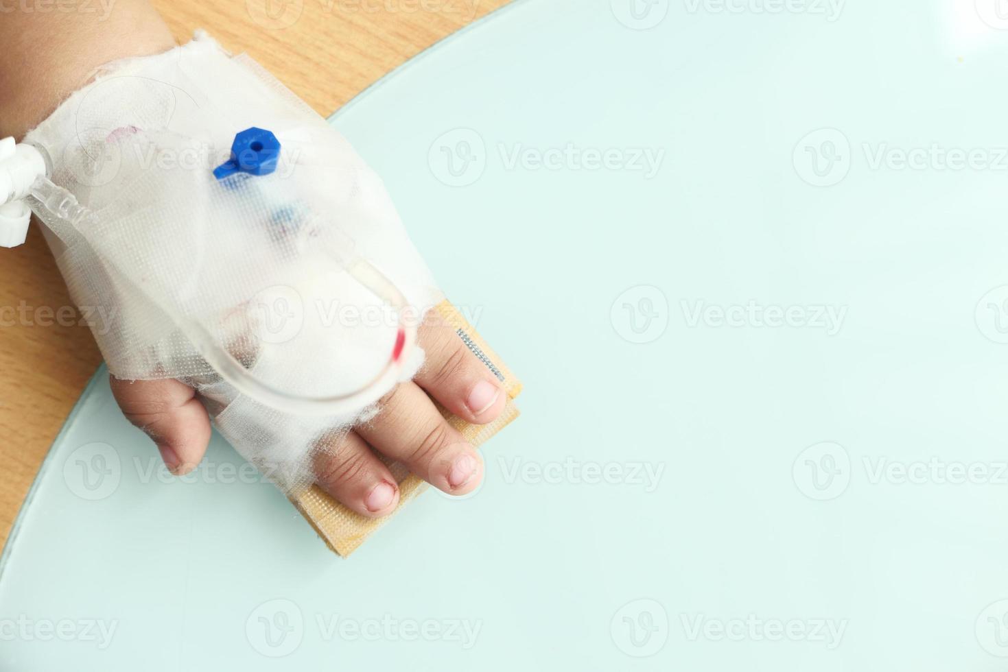 La mano del bebé con una venda dando solución salina en la cama de un hospital foto