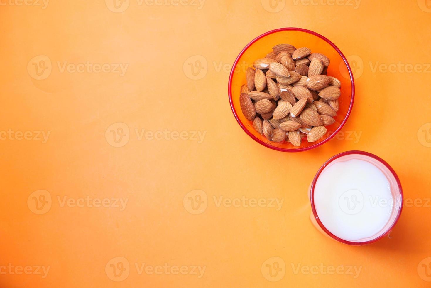 almendras y vaso de leche sobre fondo naranja foto