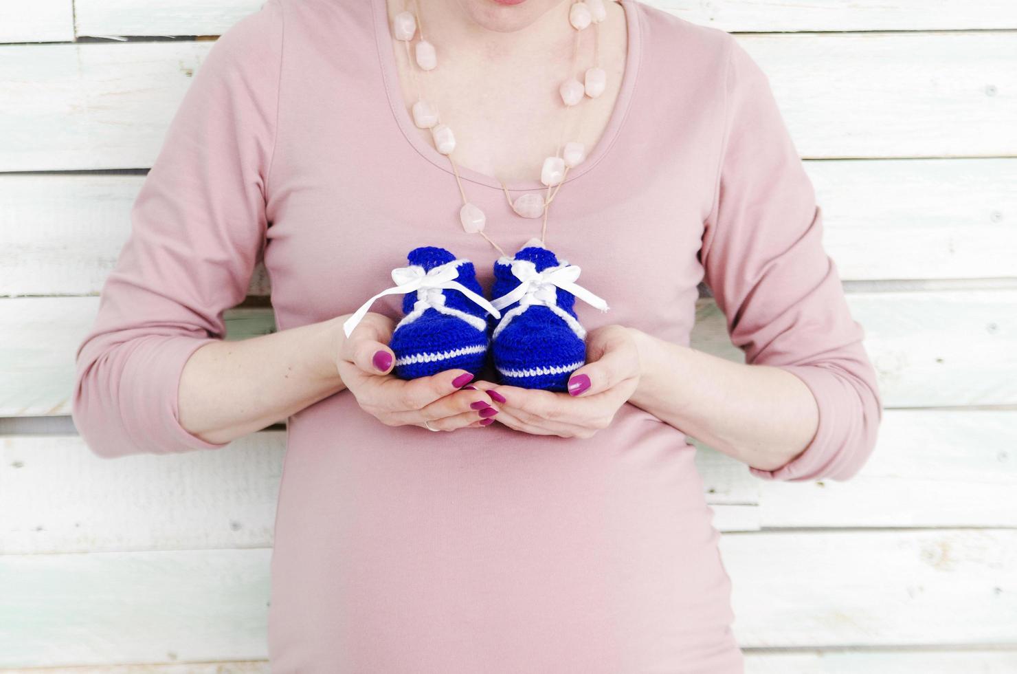 Pregnant woman holding blue baby shoes photo