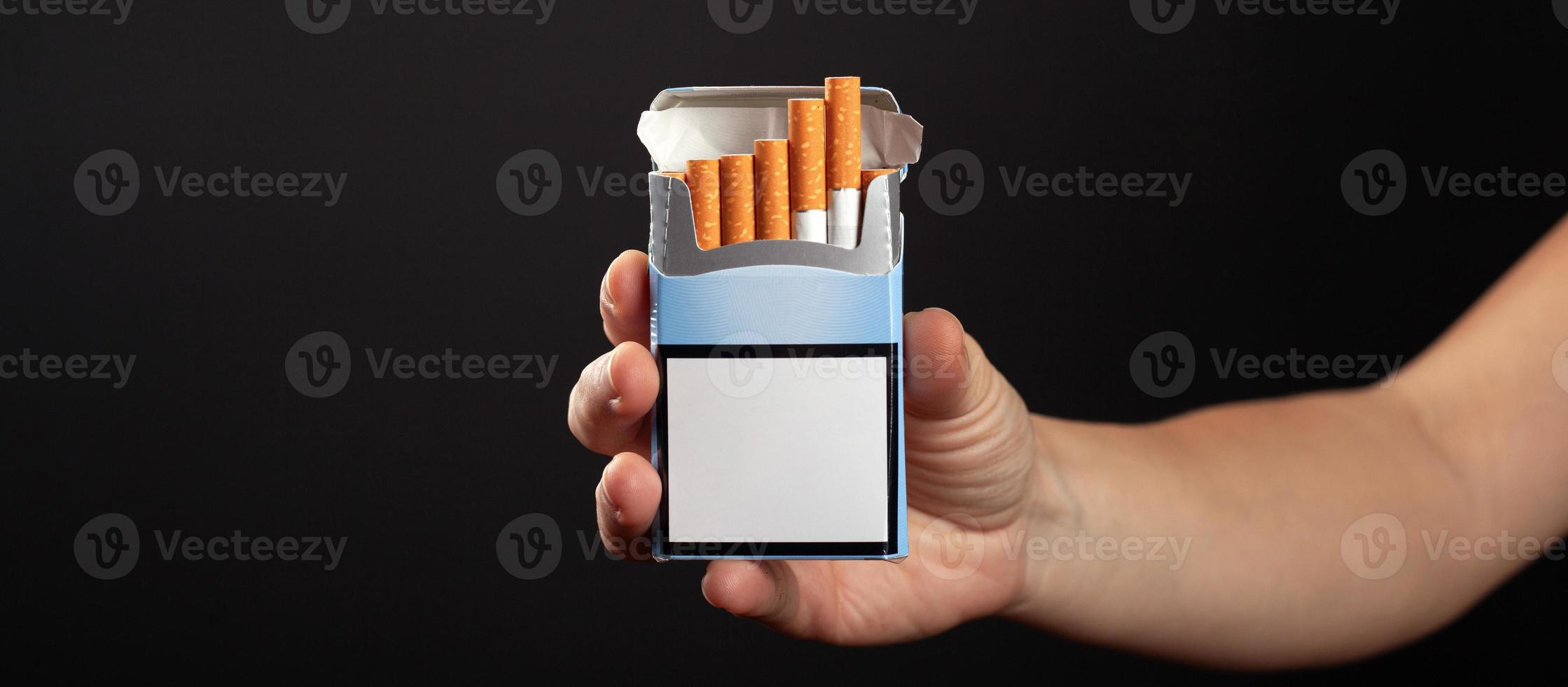 Pack of cigarettes in hand on dark background with copy space photo