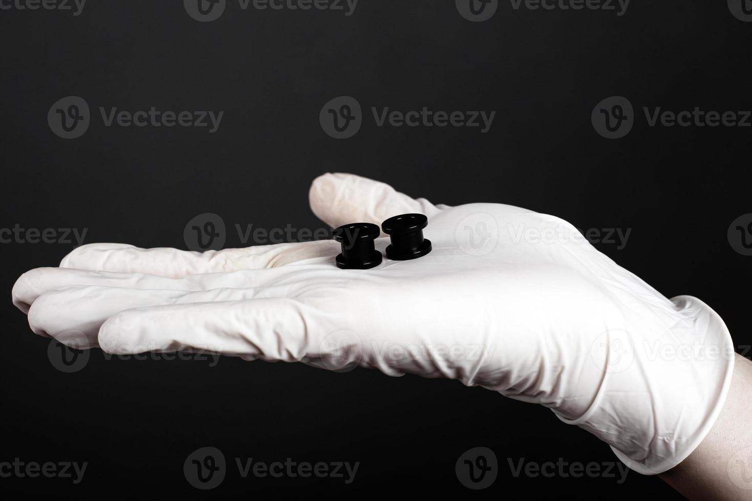 Ear jewelry, black tunnels for the ears in the palm of your hand on a dark background photo