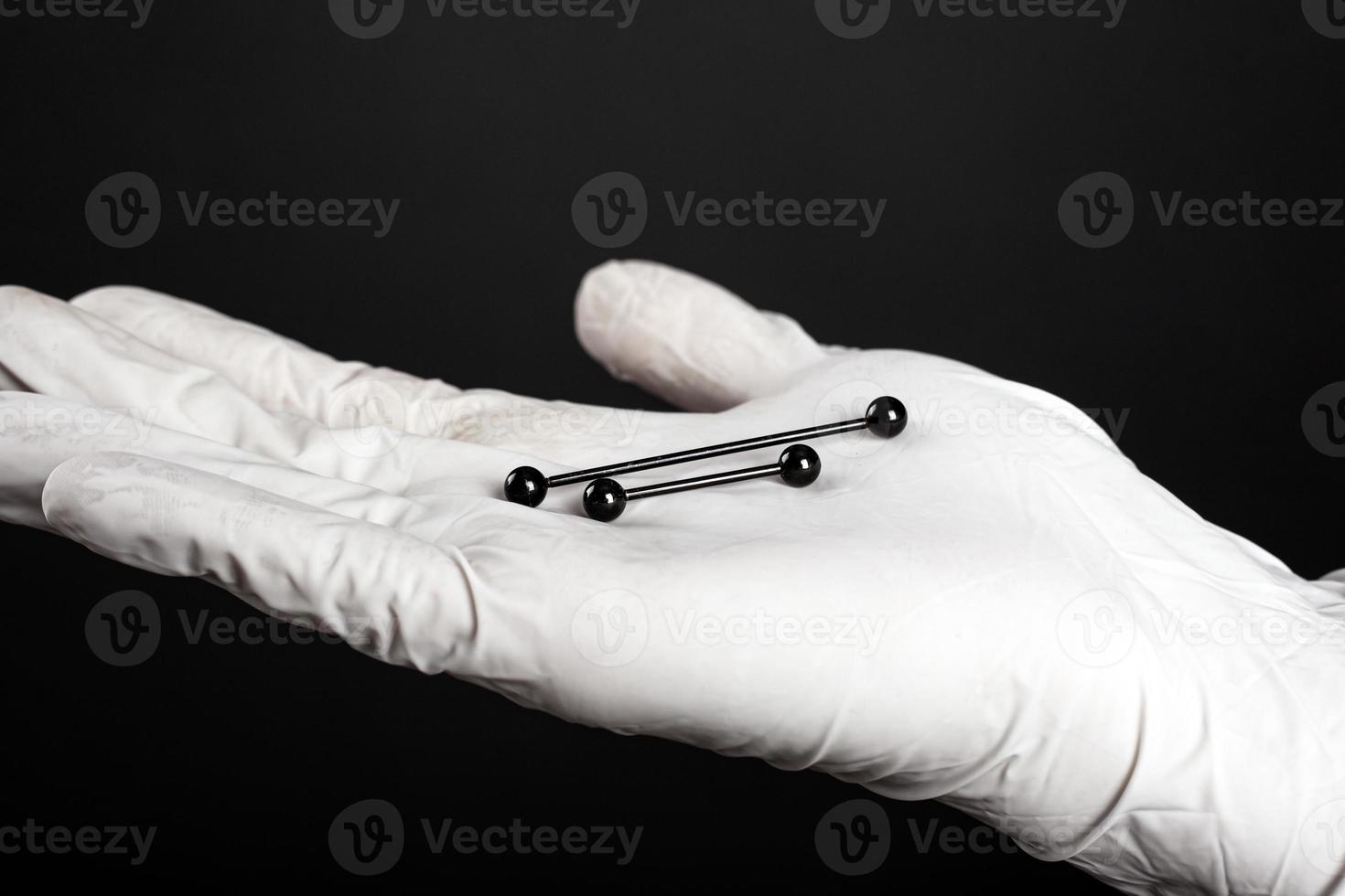 Ear jewelry, piercing in hand with a disposable glove on a dark background photo