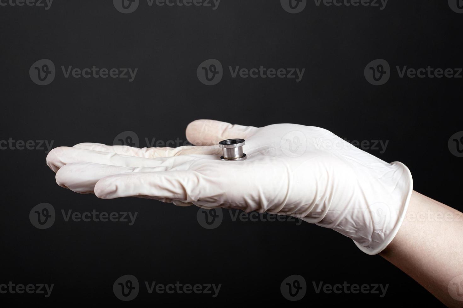 Ear jewelry, hand holds a tunnel for the ear on a dark background photo