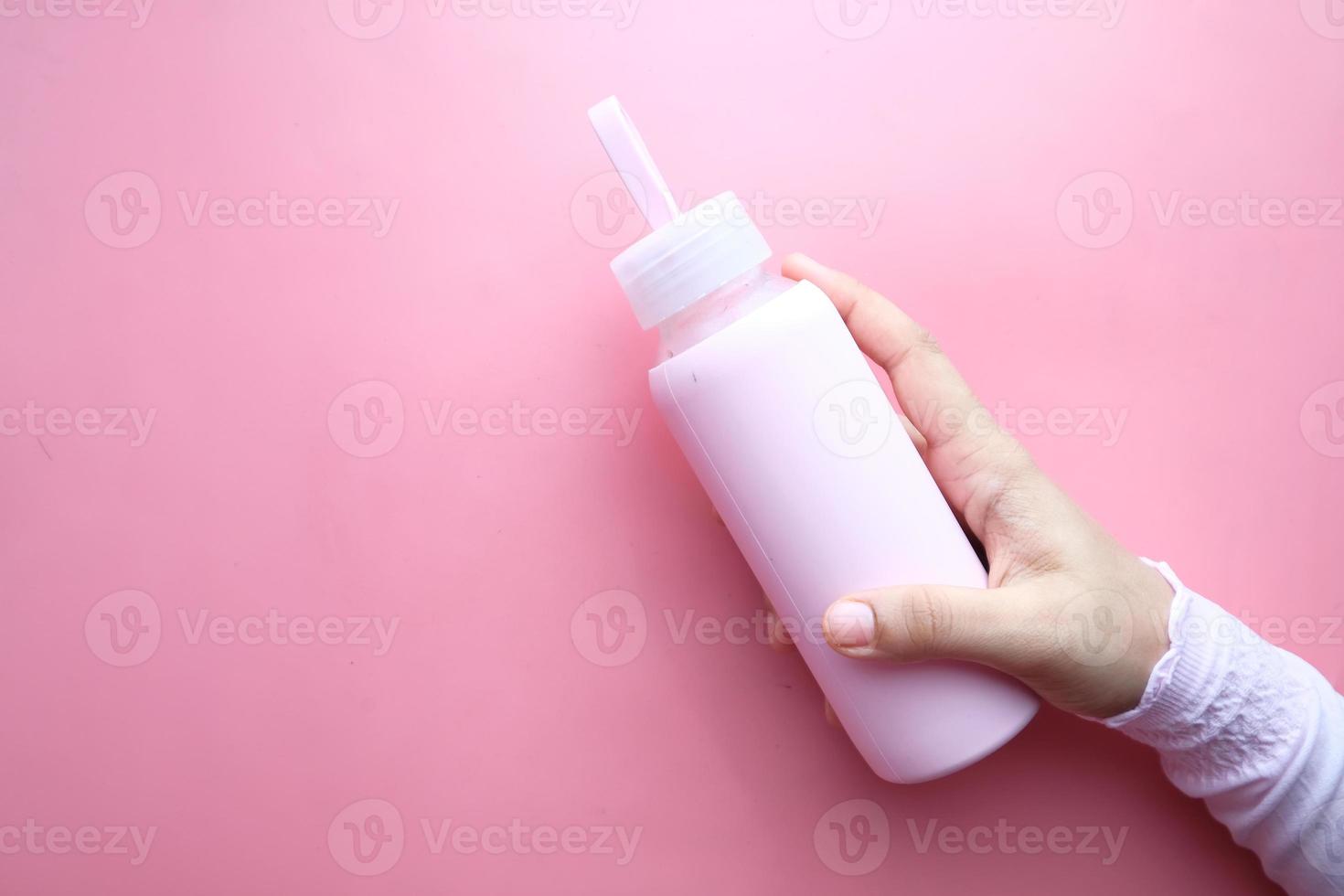 Mano sujetando una botella de agua deportiva aislada sobre fondo rosa foto