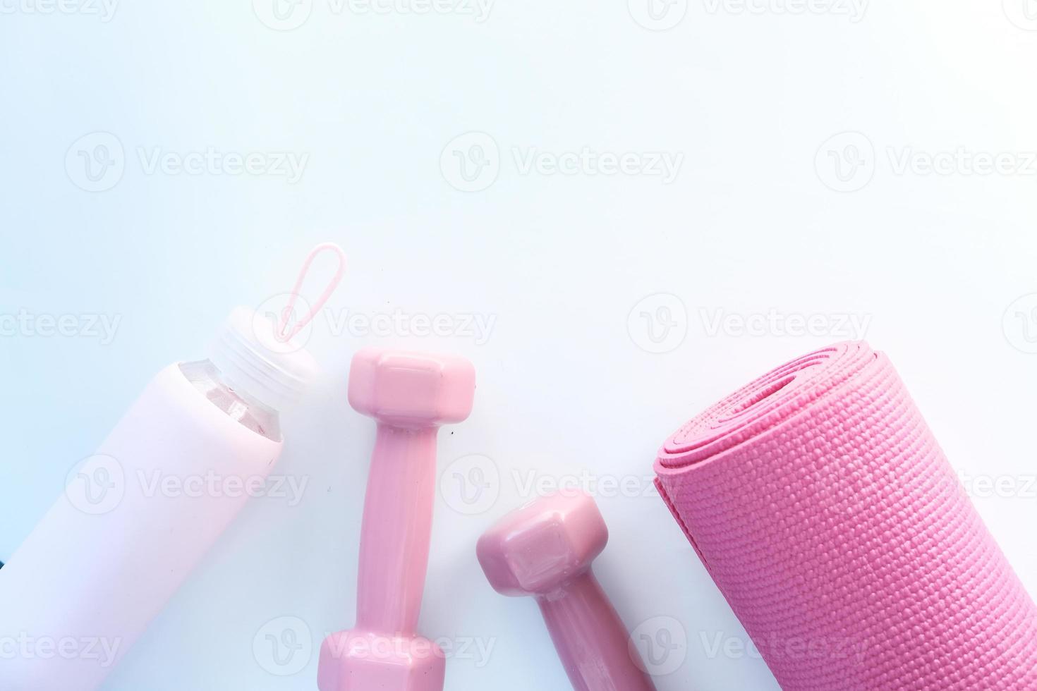 Pink color dumbbell, exercise mat, and water bottle on white background photo