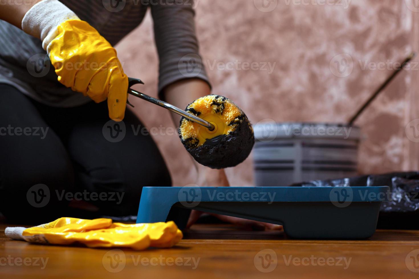 Person in yellow working gloves holds the roller over the tray with gray paint photo