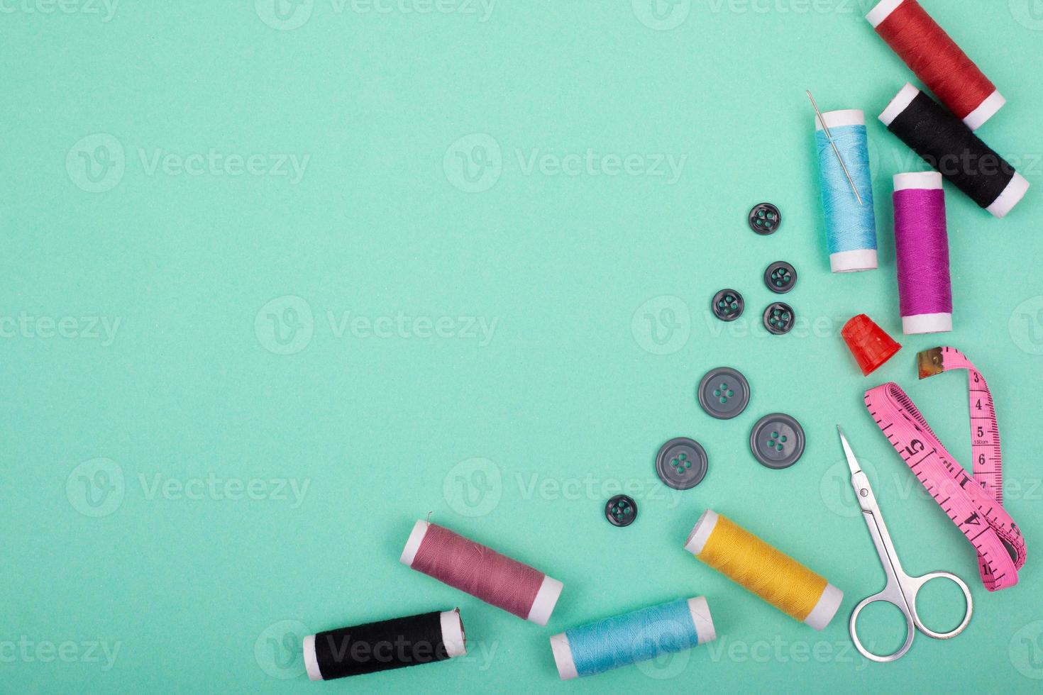 Sewing kit accessories with colorful threads, needles, pins, scissors on green background photo