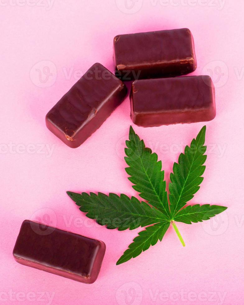 Chocolate candy with marijuana on pink background photo