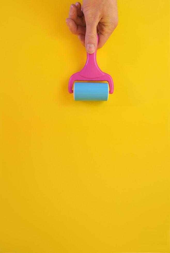 Concept of male hand holding paint roller against clean yellow background with copy space for text message. photo