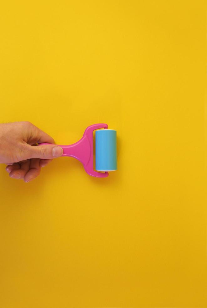 Concept of male hand holding paint roller against clean yellow background with copy space for text message. photo