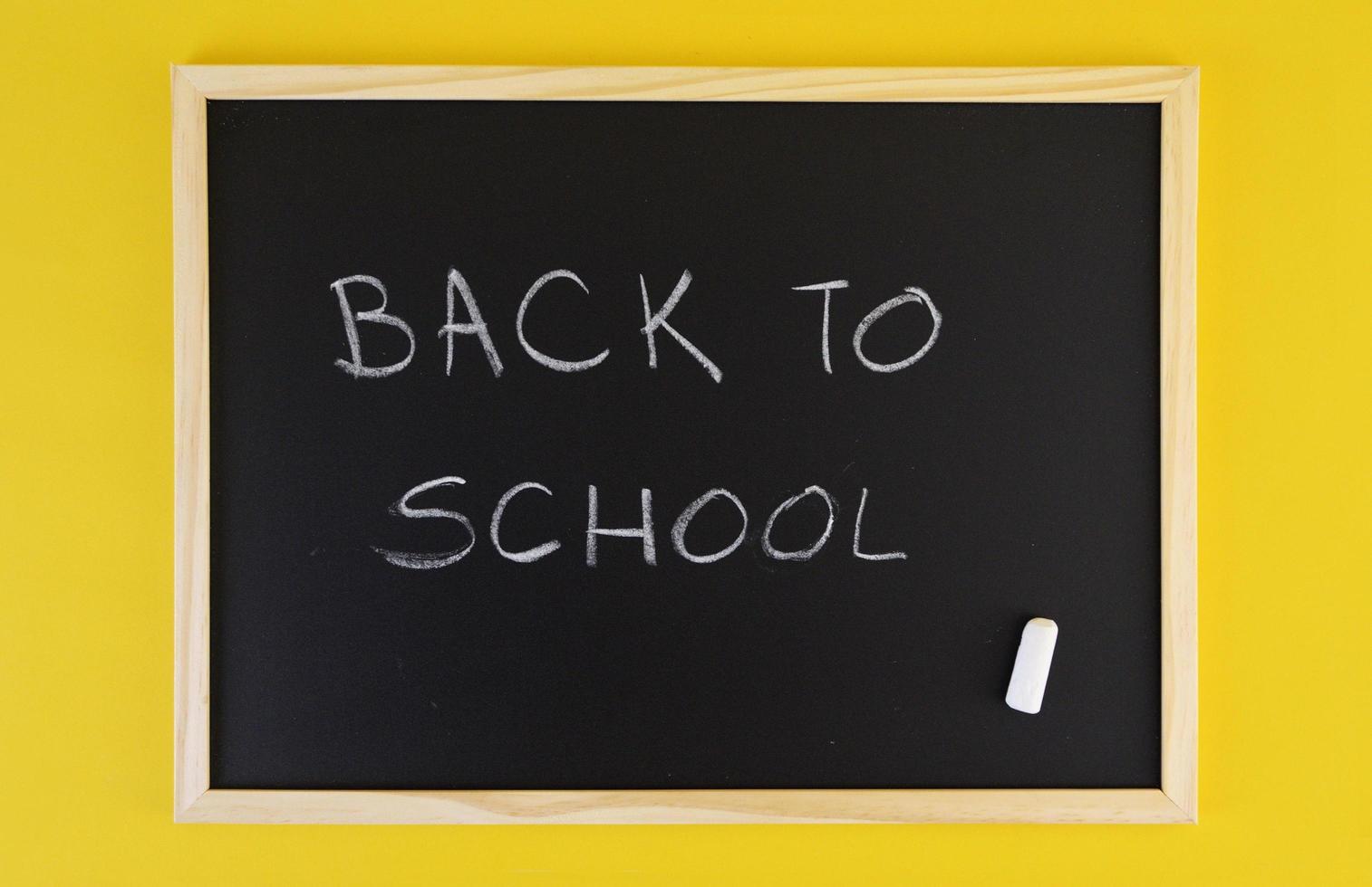 Hand-drawn title welcomes Back to School on black chalkboard among yellow vivid background. photo