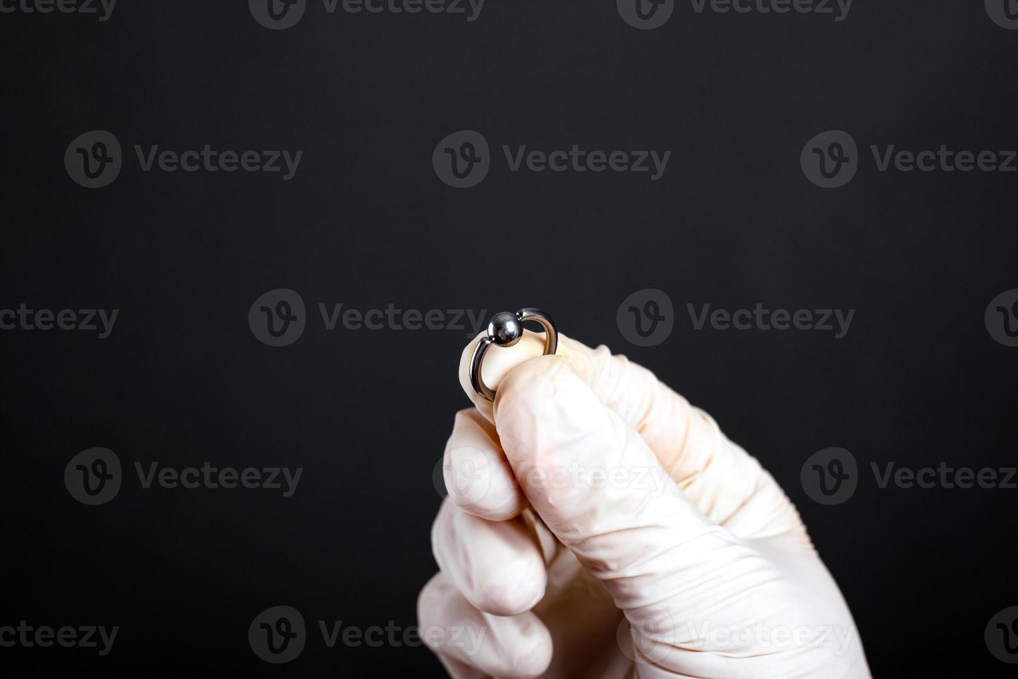 Mano en guante blanco sostiene joyas piercing sobre un fondo oscuro foto