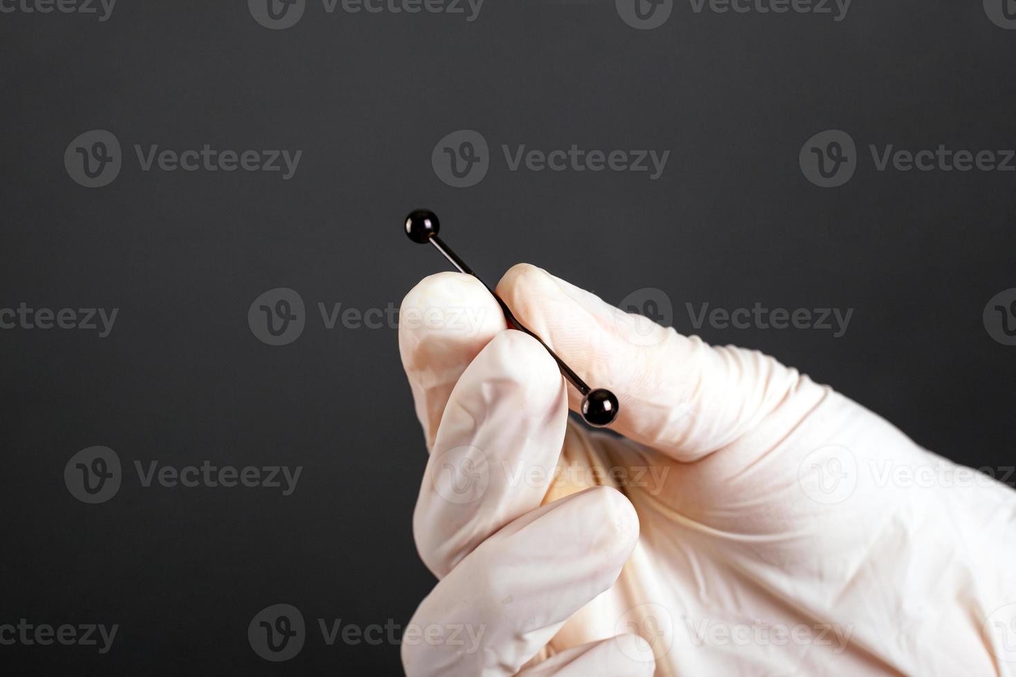 Hand in a white sterile glove holds a jewelry piercing for cartilage photo