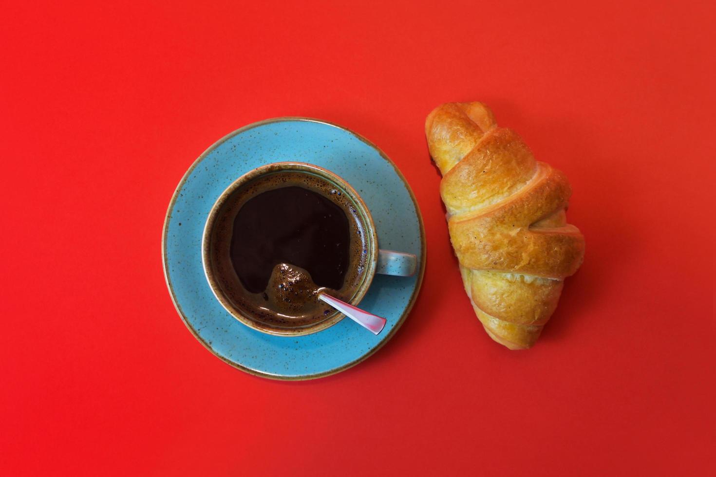 Coffee cup and fresh croissant isolated on red background with copy space. Top view on fresh breakfast with coffee and baked sweet pastries. photo