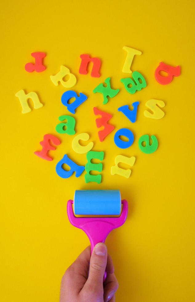 Concept of male hand holding paint roller while painting colorful letters on yellow background. photo