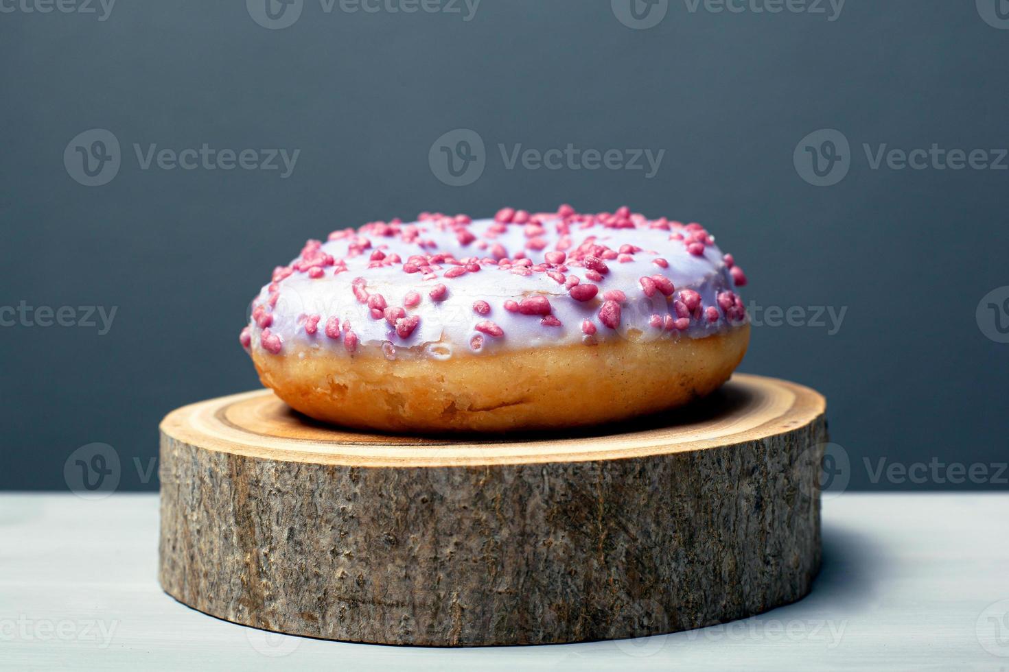 Donut en esmalte púrpura sobre un soporte de madera sobre un fondo gris foto