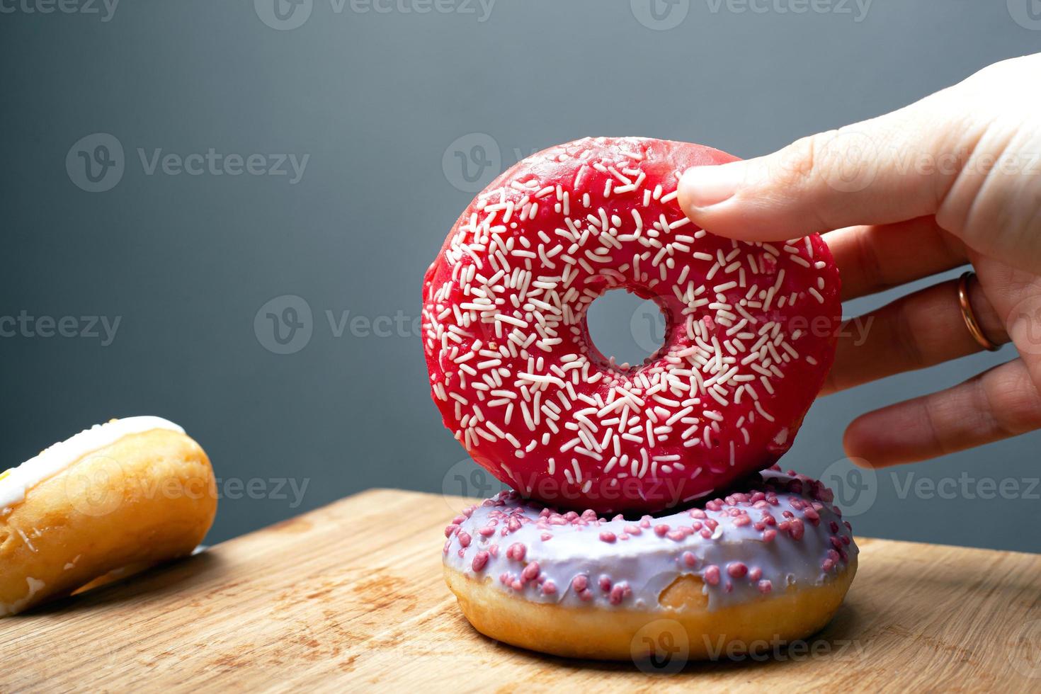 Mano femenina sostiene rosquillas de pastelería dulce con esmalte rojo y violeta sobre un fondo gris foto