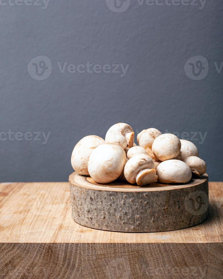 Fresh champignon greenhouse mushrooms on a rustic stand on a gray background photo