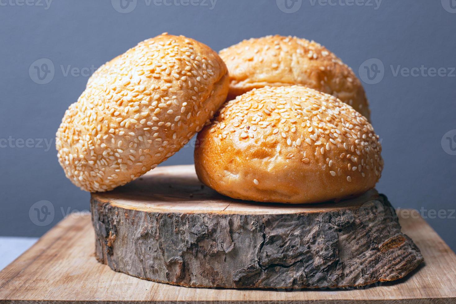 Bollos para hacer hamburguesas con semillas de sésamo sobre un soporte de madera sobre un fondo gris foto