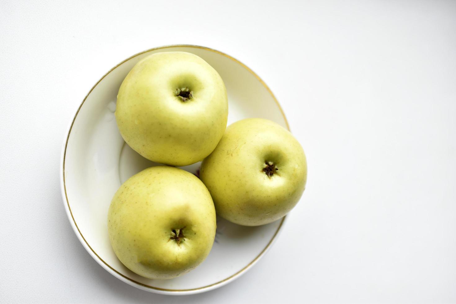 Tres manzanas verdes en una placa blanca. foto