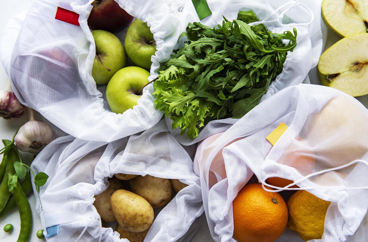 Fruits and summer vegetables in reusable eco friendly mesh bags on marble background. Zero waste shopping. Ecological concept. photo