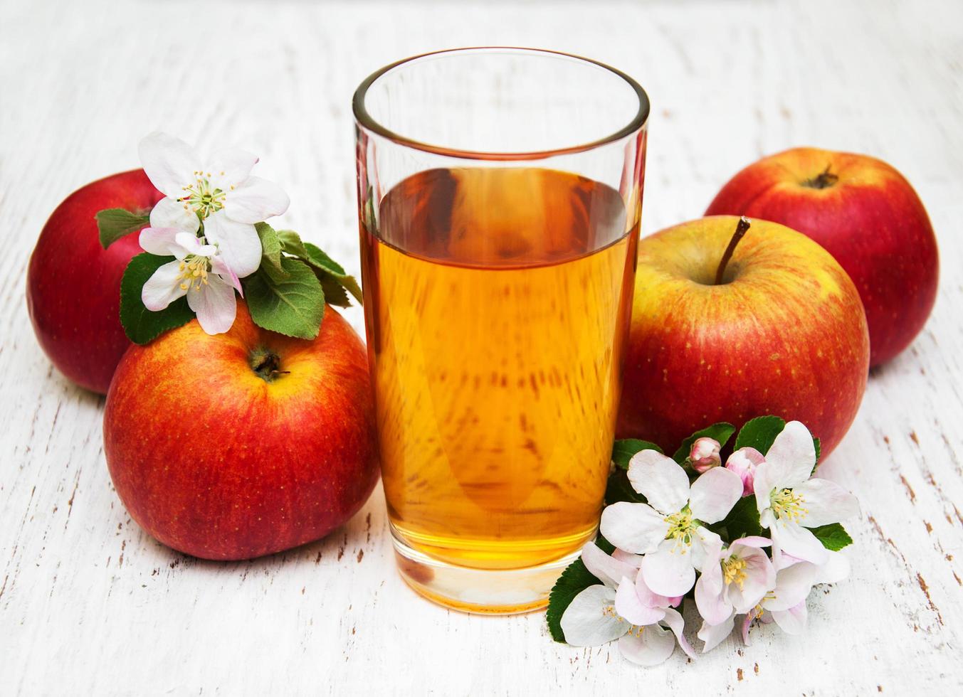 Vaso de jugo de manzana con manzanas y flores sobre un fondo de madera foto