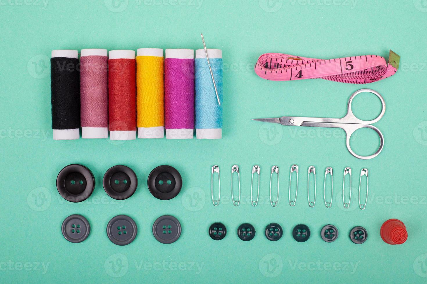 Accesorios del kit de costura con hilos de colores, agujas, alfileres, tijeras sobre fondo verde foto