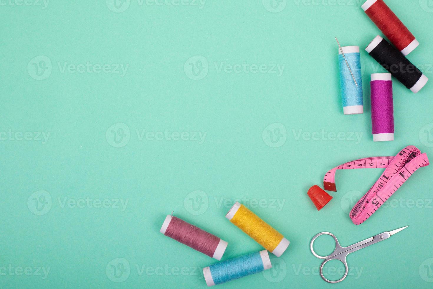 Sewing kit accessories with colorful threads, needles, pins, scissors on green background photo