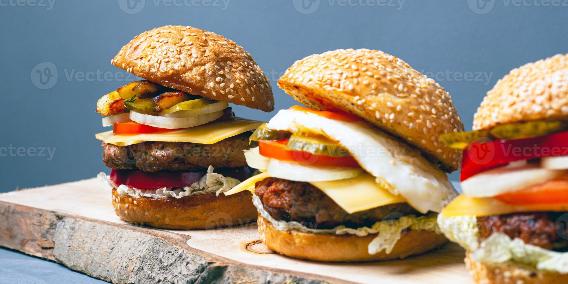 Surtido de hamburguesas con queso sobre corteza de árbol y fondo gris foto