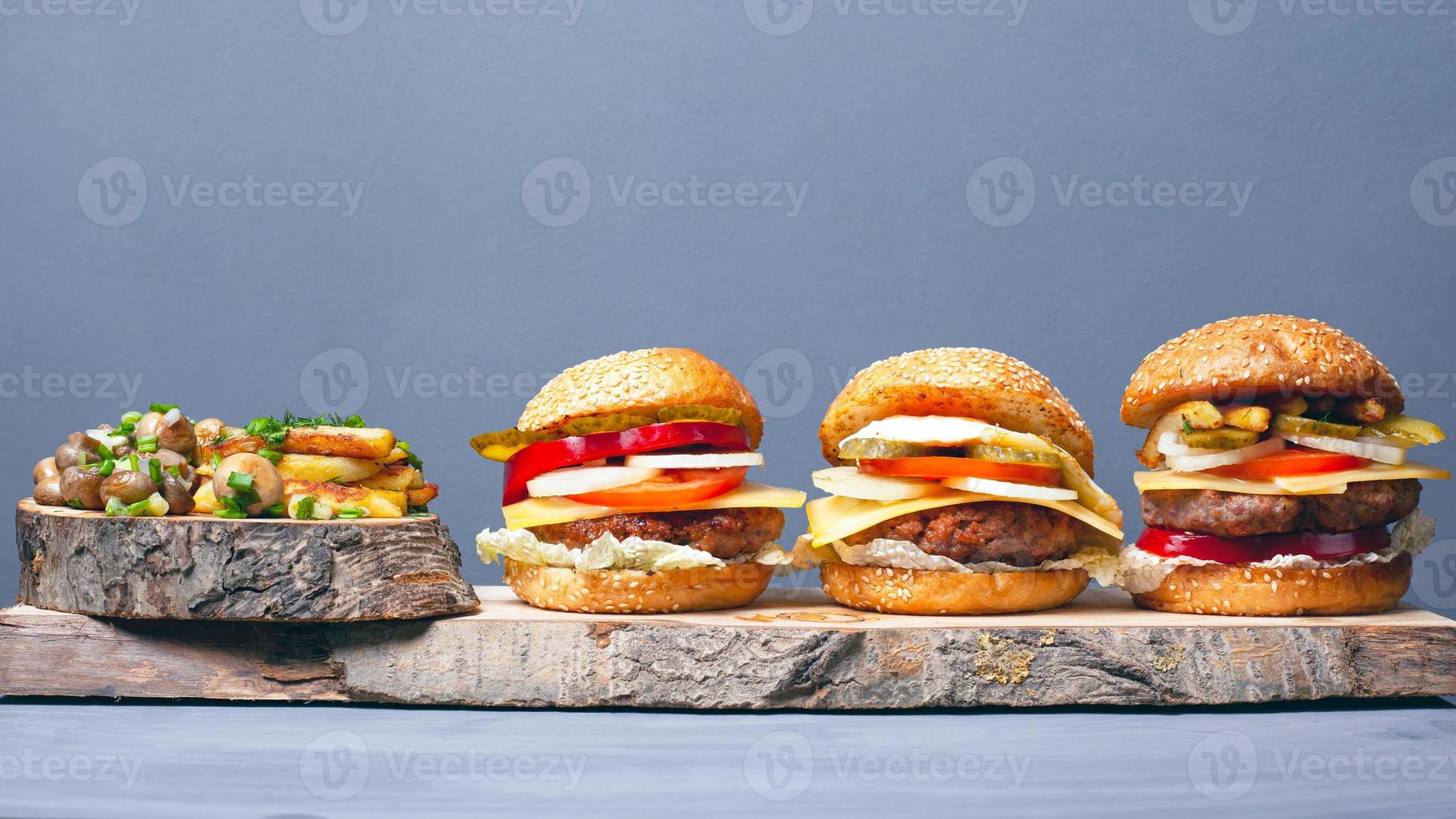 Three tasty assorted hamburgers with fries and mushrooms on a gray background photo