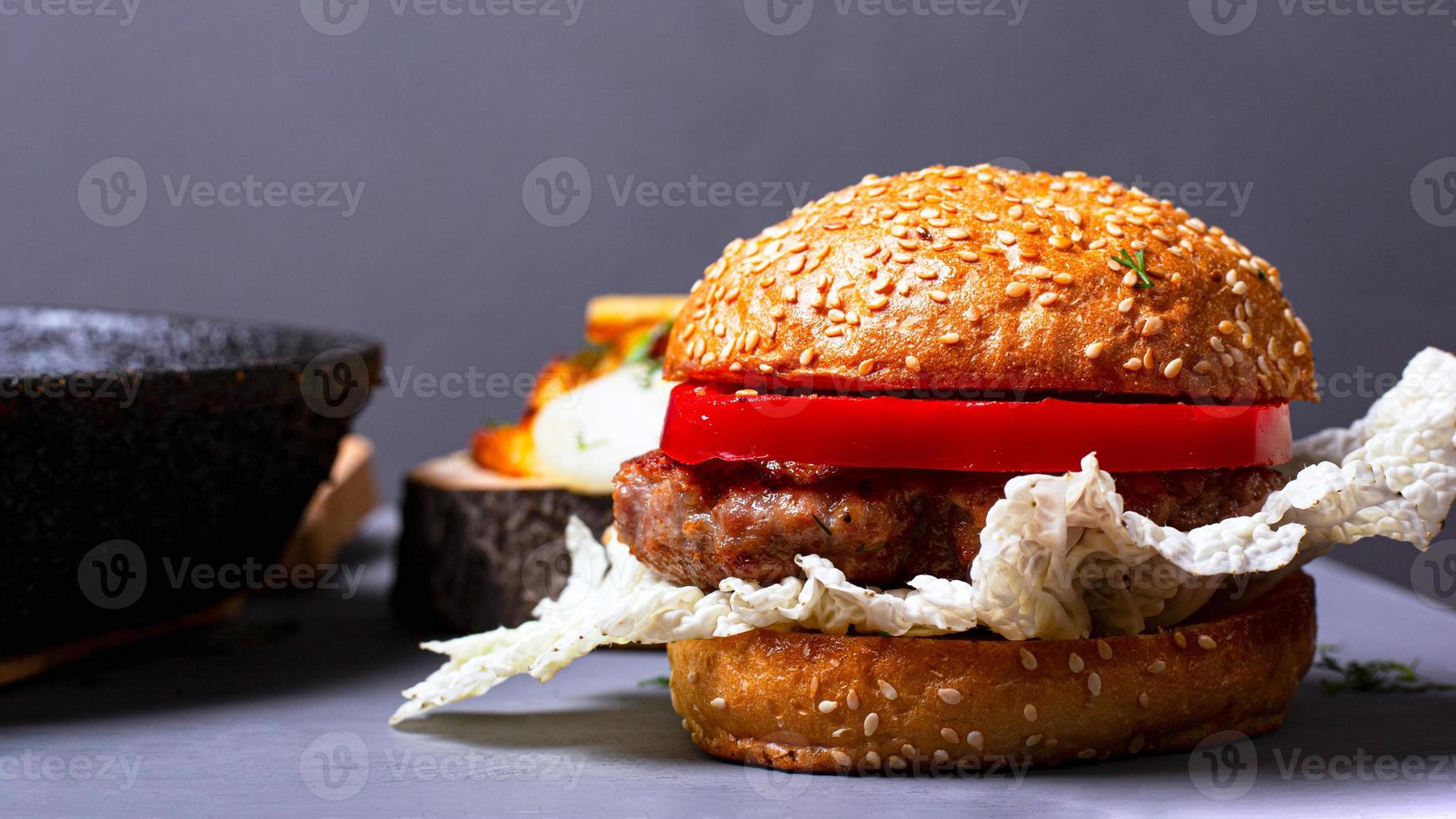 Hamburguesa clásica casera con col china, chuleta jugosa y pimiento dulce sobre un fondo gris foto