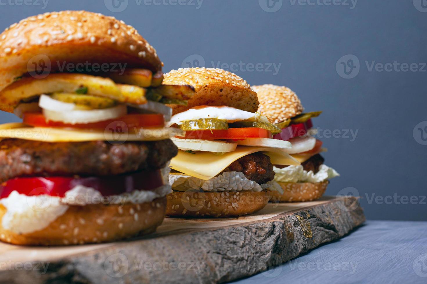 Three burgers on a wooden forest stand on a gray background photo