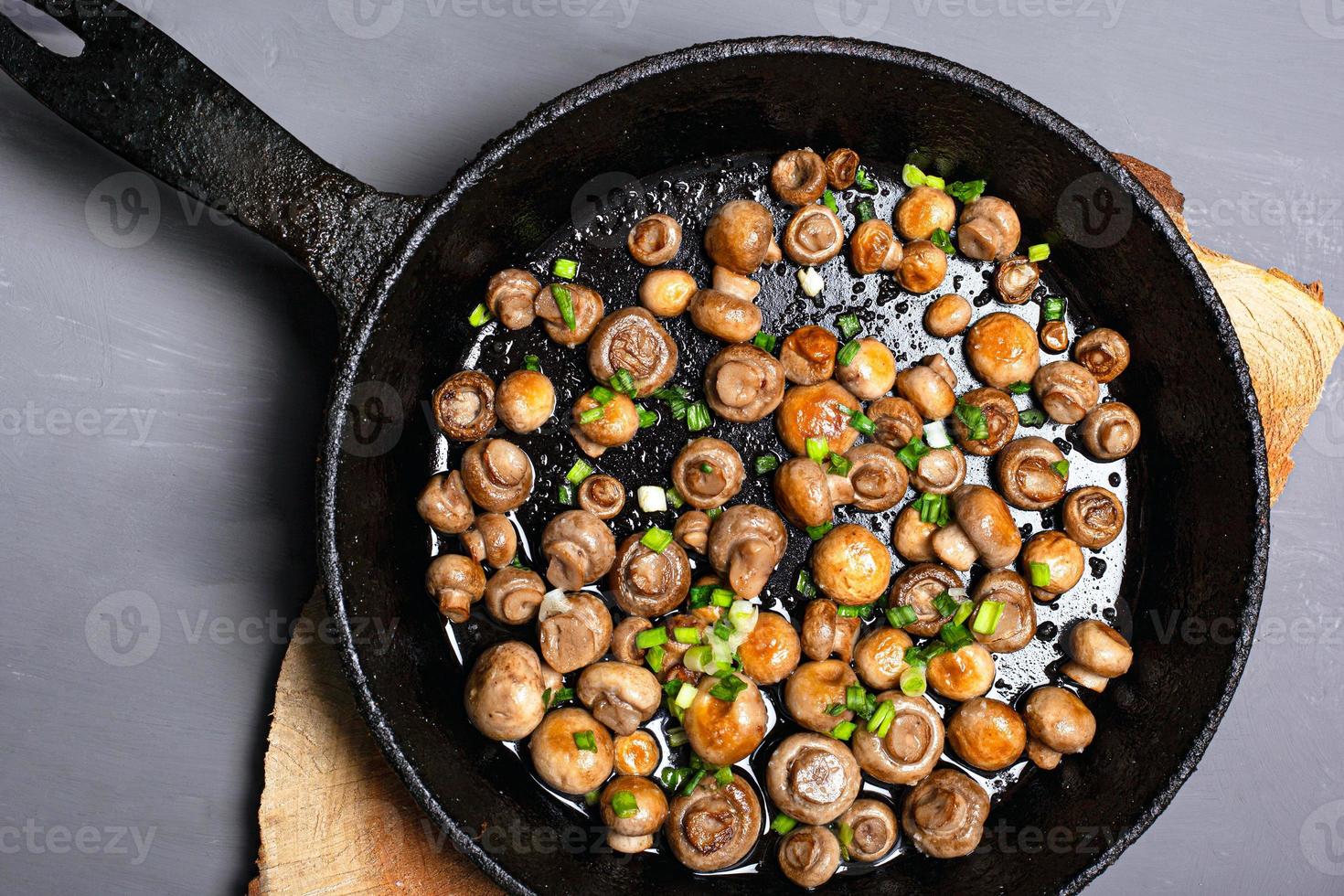 Champiñones fritos espolvoreados con hierbas en una sartén negra sobre un fondo gris foto