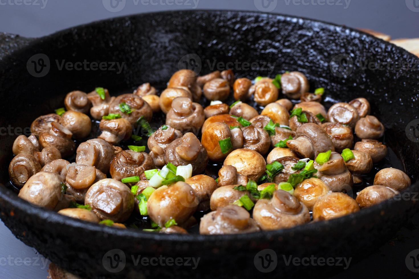 Champignon mushrooms fried to golden color with green onions in a pan close-up photo