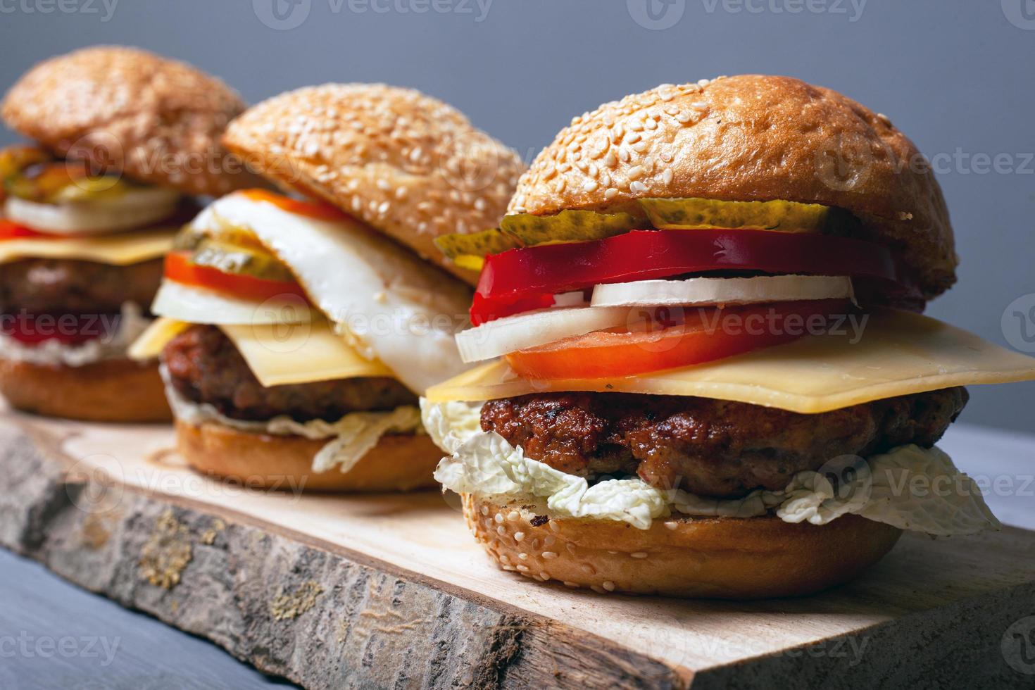 Tasty homemade burgers on a wooden stand on a gray background, side view photo