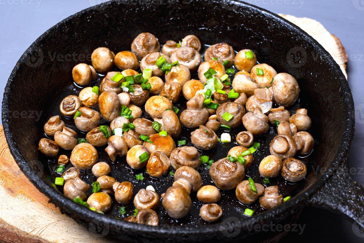 Champiñones fritos con cebollas verdes en una sartén de hierro fundido sobre un soporte de madera foto