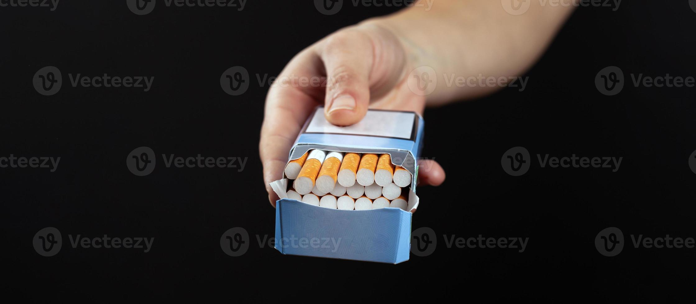 Pack of cigarettes in hand on dark background with copy space photo