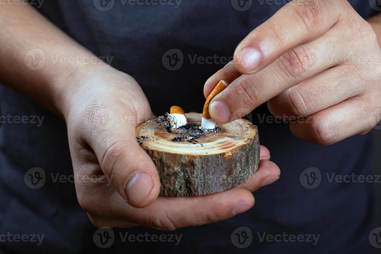 Male hands put out a cigarette butt on a wooden forest stand photo